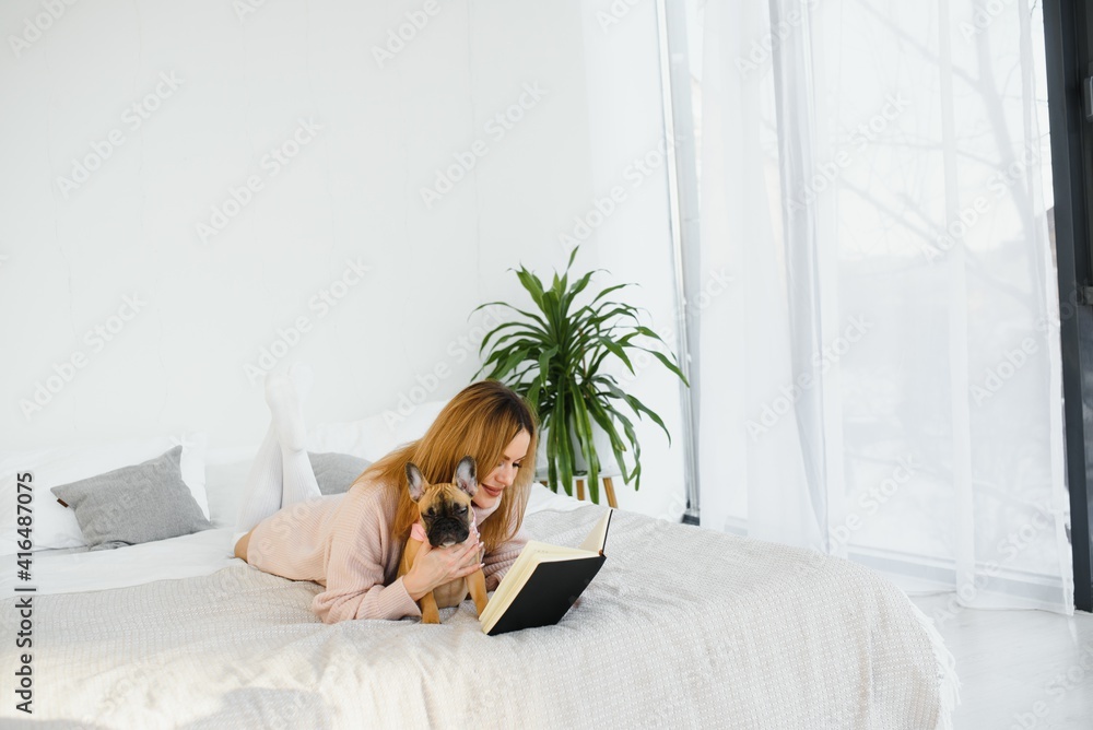 Cheerful young woman holding her big puppy with black nose and laughing. Indoor portrait of smiling girl posing with french bulldog Cheerful young woman holding her big puppy with black nose and laughing. Indoor portrait of smiling girl posing with french bulldog