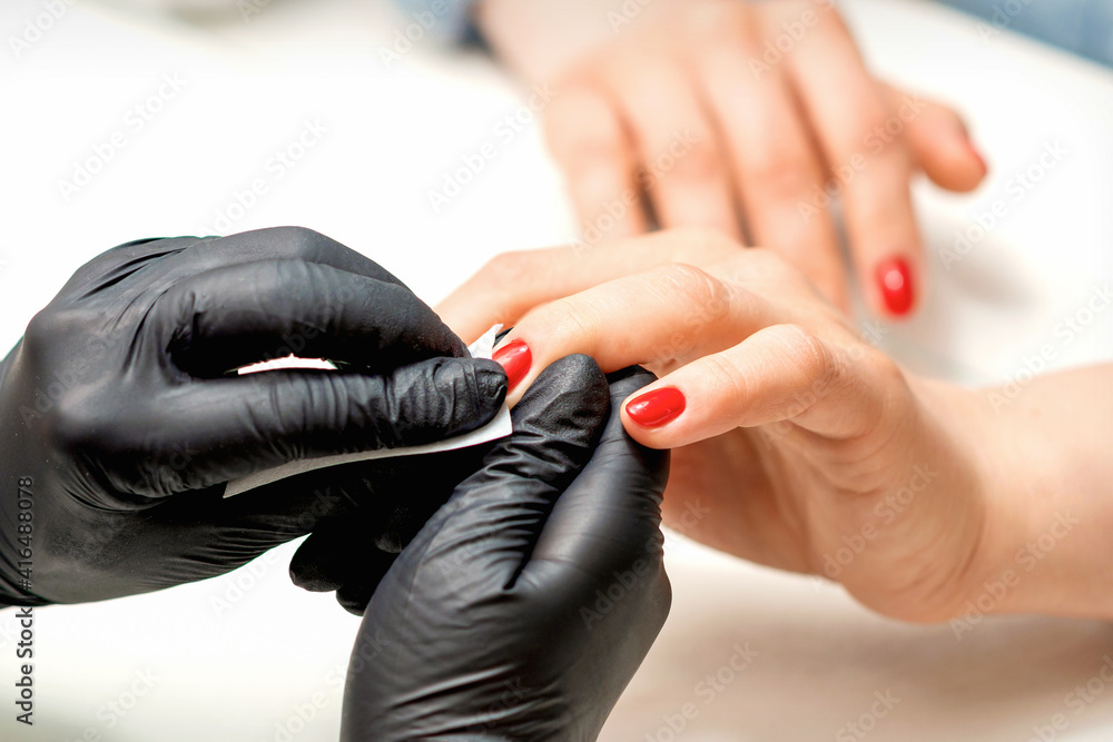 Close up of manicure master leaks female red nails with a lint-free napkin in a nail salon Close up of manicure master leaks female red nails with a lint-free napkin in a nail salon