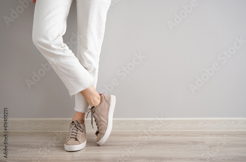 Legs of a young girl in jeans and sneakers on a gray background, space for text.