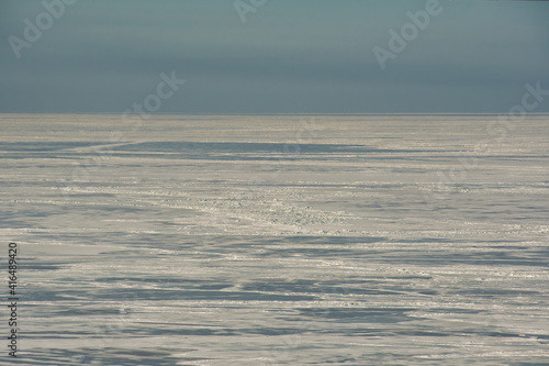 The icy desert that the winter-frozen Gulf of Finland has become  under the sky in a cloudy haze in direct sunlight.