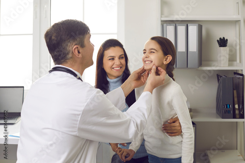 Dentist examines little patient. Happy smiling kid shows good white healthy even teeth to hygienist. Mom and child seeing orthodontist to fix bite and align jaws correctly at early age, in childhood