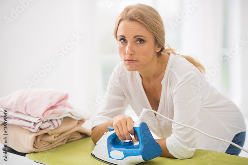 Woman standing near the ironng table and looking sad