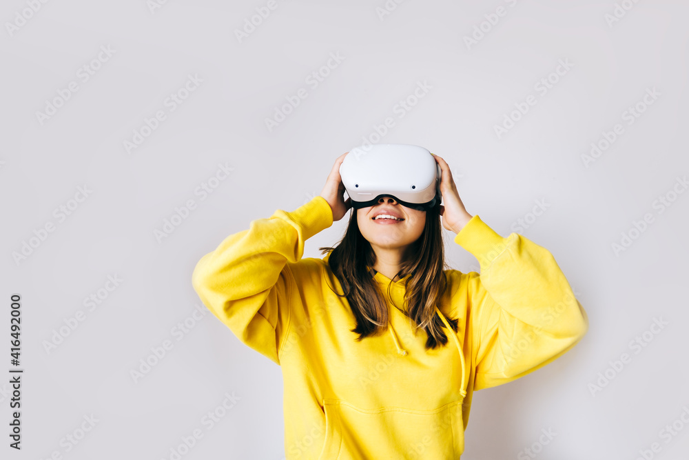 Young caucasian woman using VR headset, touching glasses and looking up in virtual reality on white background.