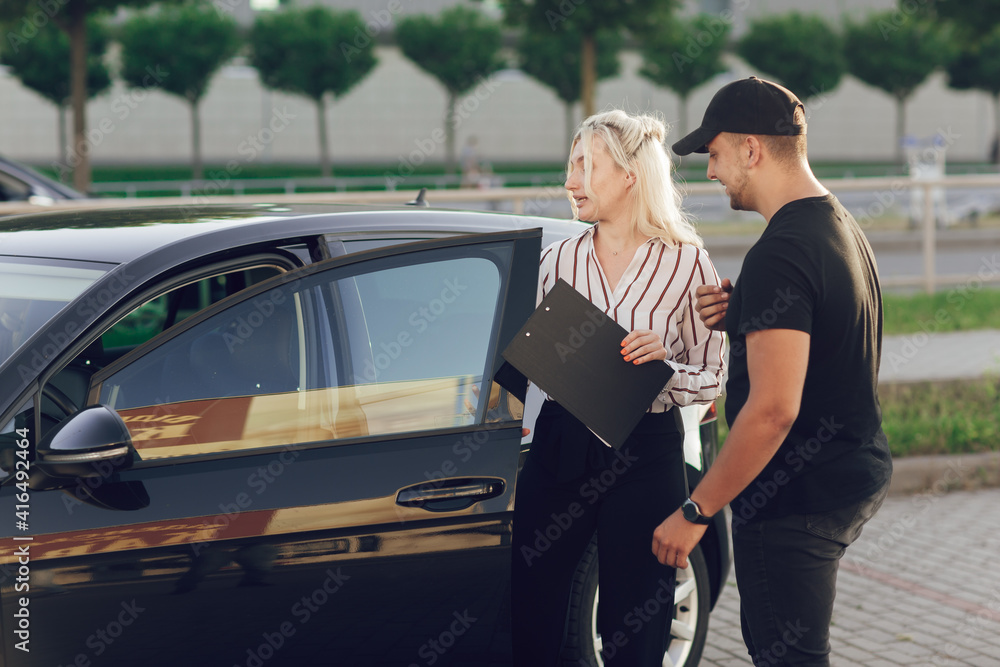 Young blond woman consultant in show room shows the customer the car outdoors. A man buys a car. Test drive a new car