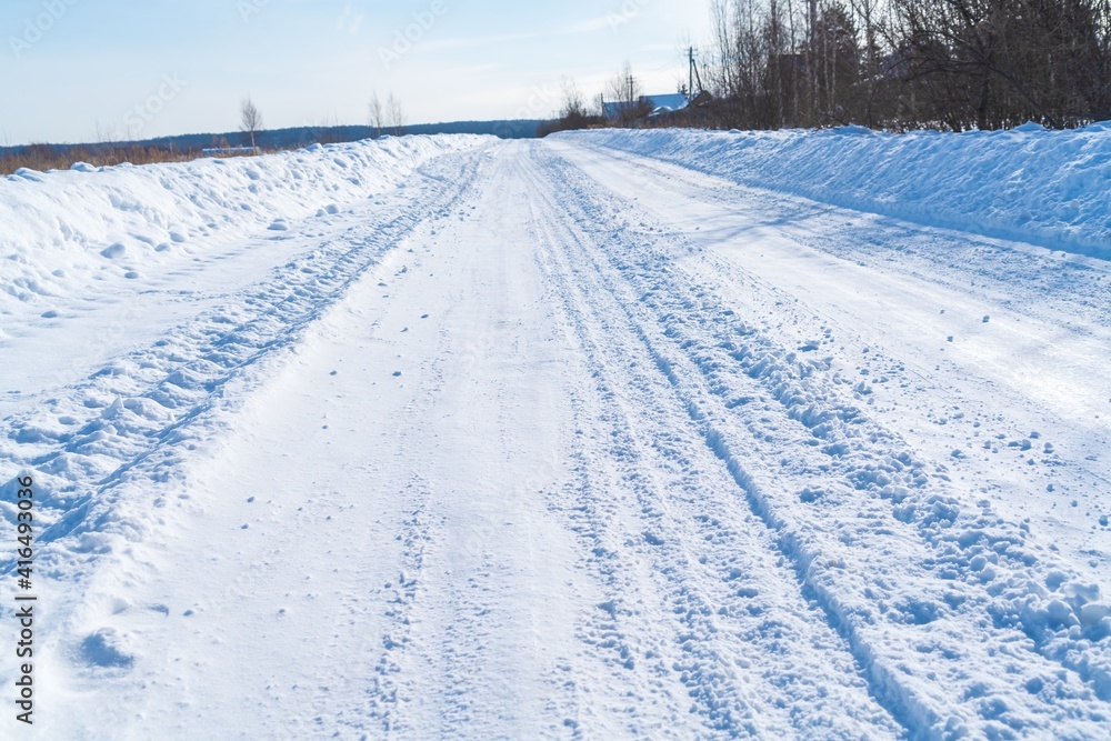 Rural road in winter covered with rolled snow on the background of snow-covered fields and forests with a clear sky