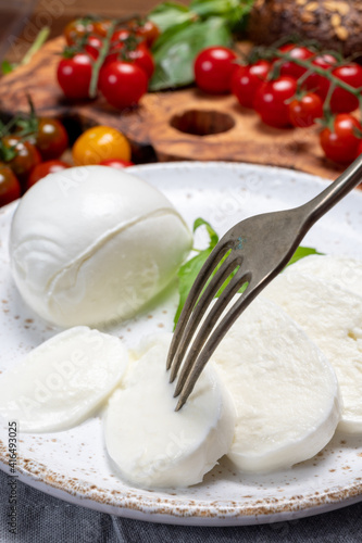 Cheese collection, eating. of white soft Italian cheese mozzarella, served with red cherry tomatoes, fresh basil leaves