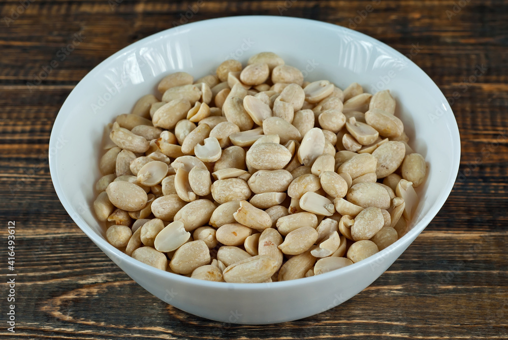 Peanuts in a white bowl on an old shabby board. Nuts on a brown wooden table.