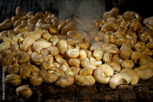 Cashew close up. Texture of nuts. Lots of nuts in a pile. Contrasting dramatic light as an artistic effect. Smoke and steam from roasting seeds in the background.
