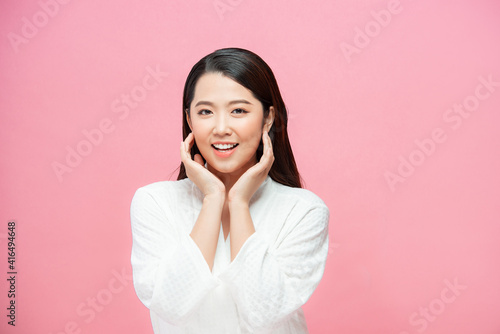 Portrait of beautiful young brunette with bare shoulders touching her cheeks and looking at camera, on pink background © makistock