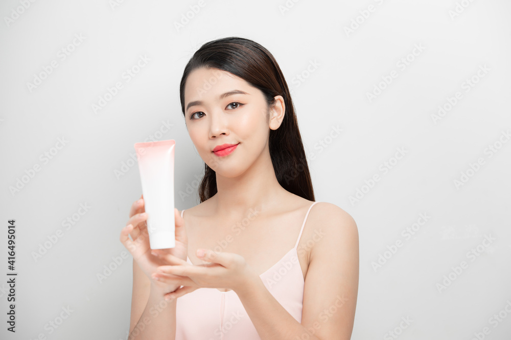 Beautiful woman shows the bottle of skincare on a gray background. Beautiful woman shows the bottle of skincare on a gray background.