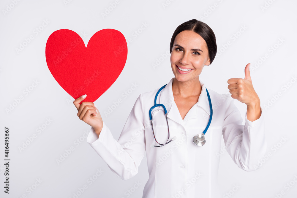 Photo of sweet charming young woman medic back wear formal coat holding red paper heart thumb up isolated white color background Photo of sweet charming young woman medic back wear formal coat holding red paper heart thumb up isolated white color background