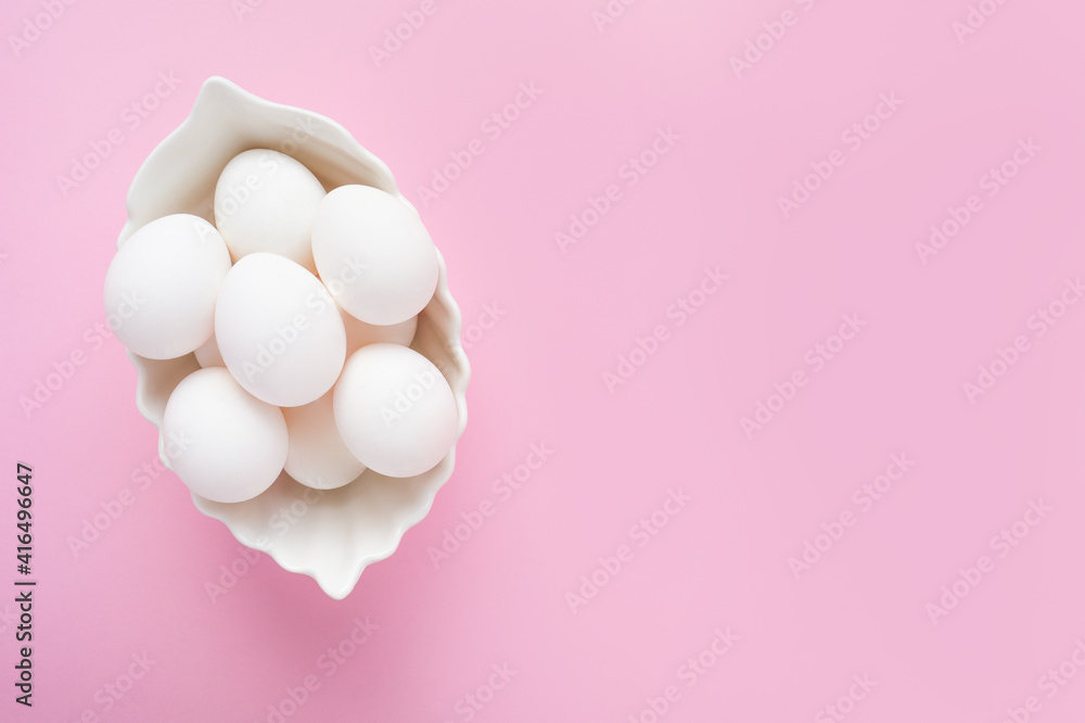 Many white eggs in a white dish on a pink background. Easter. Top view, copy space