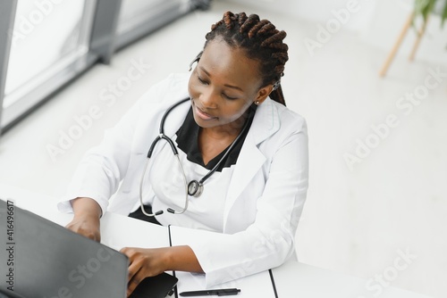 African American woman doctor working at her office online using portable inormation device. Telemedicine services. Primary care consultations, psychotherapy, emergency services. photo