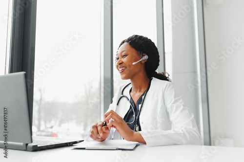 African American woman doctor working at her office online using portable inormation device. Telemedicine services. Primary care consultations, psychotherapy, emergency services. photo