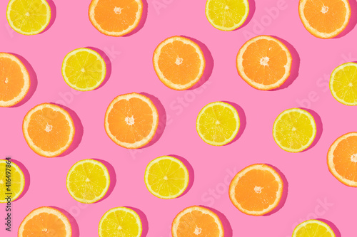 Creative pattern made with orange and lemon slices on bold pink background. Minimal flat lay. Spring or summer trendy concept. Fun idea with citrus fruits.
