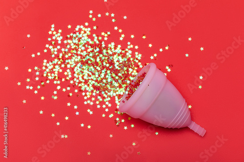 Hygienic menstrual cup cap in spray of puddle of shining stars on bright red background, symbol of blood. Studio shot flat lay, top view.