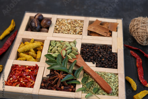 Fototapeta Naklejka Na Ścianę i Meble -  Indian spices for Indian cooking Masala hot spicy curry  whole spices turmeric, cardamom, black pepper in wooden spoon curry leaves paprika in Indian spice box Kerala India Sri Lanka.