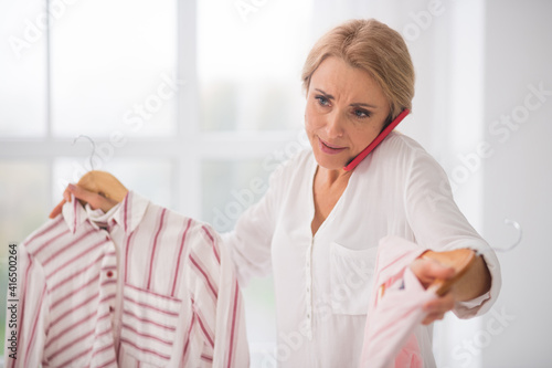Indecisive woman with clothes talking on smartphone.