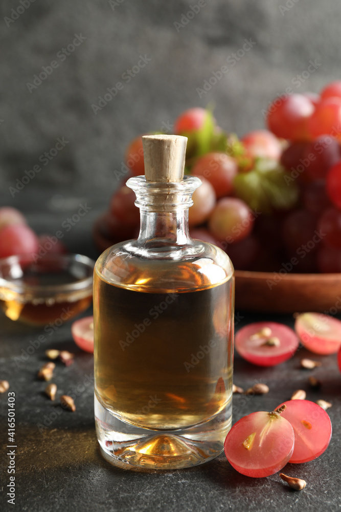 Organic red grapes, seeds and bottle of natural essential oil on black table Organic red grapes, seeds and bottle of natural essential oil on black table