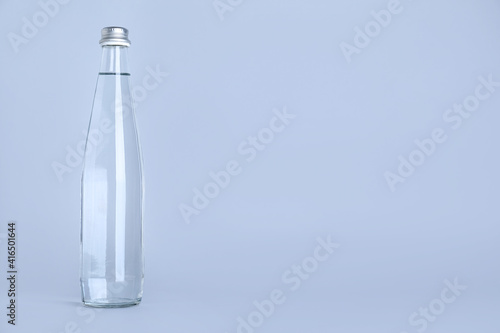 Glass bottle with water on light grey background, space for text