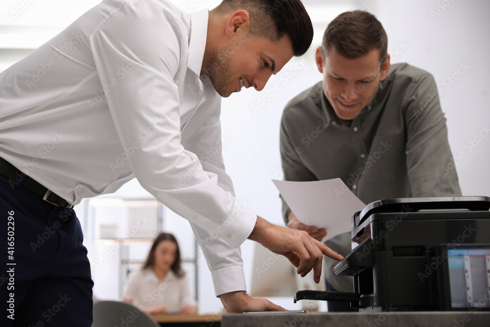 Employees using new modern printer in office Employees using new modern printer in office