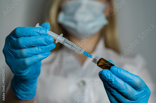 Doctor drawing up solution from vaccine bottle into syringe for vaccination