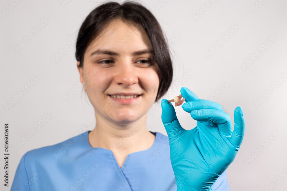 Dentist holding ceramic artificial false unit tooth. Dental prosthesis in gloved hands of the doctor close-up. Dentistry conceptual photo. Prosthetic dentistry. False teeth