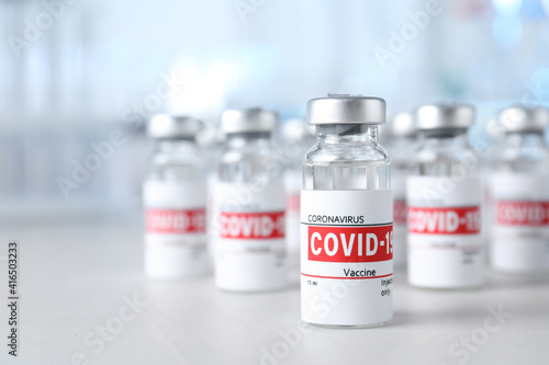 Glass vials with COVID-19 vaccine on light table. Space for text