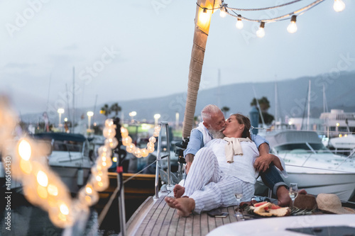 Senior couple having tender moment on boat while drinking champagne and eating fruits - Focus on faces