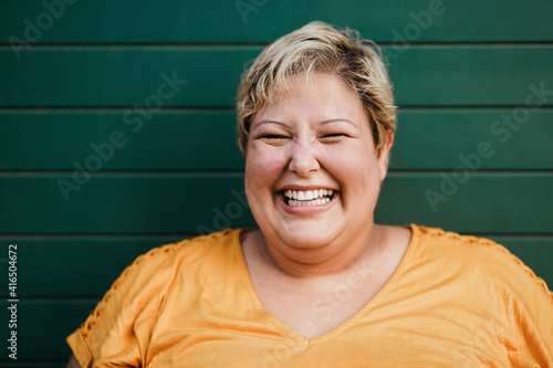 Portrait of curvy woman smiling on camera outdoors with green background - Focus on face