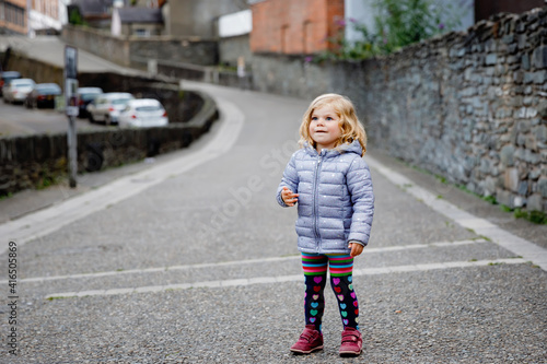 Beautiful portrait of cute little toddler girl. Happy baby child looking at the camera and smiling. Kid making a walk through historical old town. Outdoors at the dusk.
