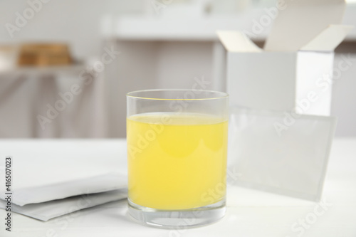 Glass with dissolved drug and medicine sachets on table indoors