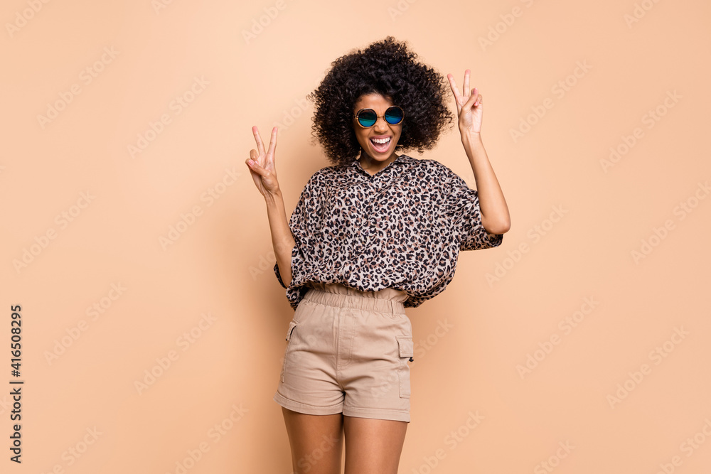 Photo portrait of cheerful curly woman showing v-sign gesture in sunglass isolated on pastel beige color background Photo portrait of cheerful curly woman showing v-sign gesture in sunglass isolated on pastel beige color background