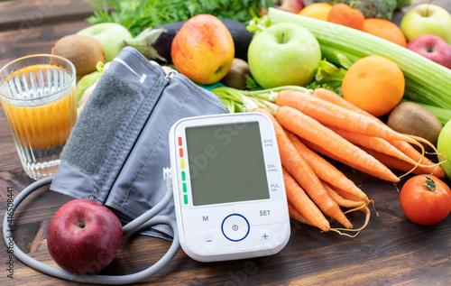 Blood pressure monitor and fresh fruits with vegetables against wooden table. Healthy lifestyle and prevention of hypertension concept
