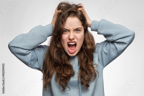 Obraz na plátně The young woman is angry and screaming, holding her head