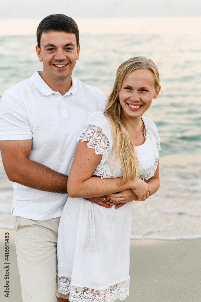 happy girl with a guy hug while walking along the beach near the ocean. romantic walk. husband and wife laugh and hug near the sea. summer rest. vacation of a young couple.