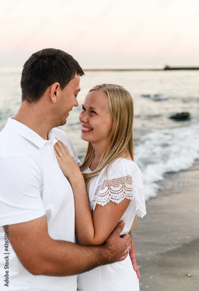 a guy with a girl in summer clothes are walking by the ocean. husband and wife at a romantic sunset of the day near the sea. lovers run along the beach. honeymoon for the newlyweds. a guy with a girl in summer clothes are walking by the ocean. husband and wife at a romantic sunset of the day near the sea. lovers run along the beach. honeymoon for the newlyweds.