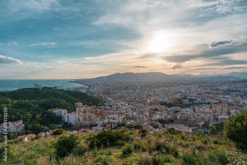 beautiful views from the top of the hill over the city of Malaga with the mountains, the sea and the cloudy sky in the background at sunset