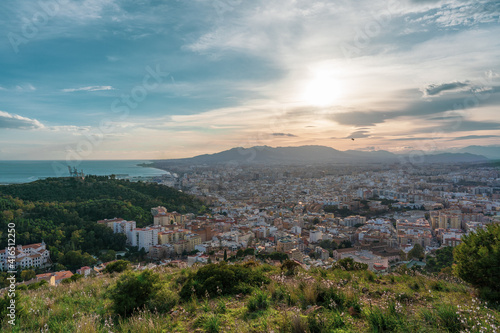 beautiful views from the top of the hill over the city of Malaga with the mountains, the sea and the cloudy sky in the background at sunset © victor
