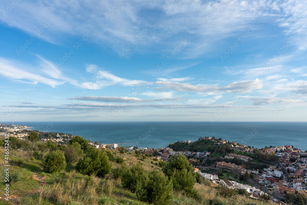 view of the city and the sea from the top of the hill with the cloudy sky in the background