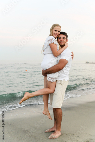beautiful girl with white hair kisses her husband on the cheek on the beach near the ocean at sunset. romantic walk. vacation of a young family. travel to the sea.