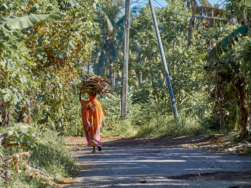 Comorian woman carrying brushwood on her head in traditional orange dress.