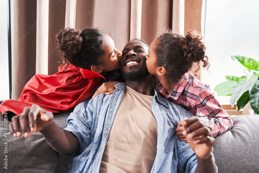 Obraz premium Father sitting at the sofa while his daughters kissing him
