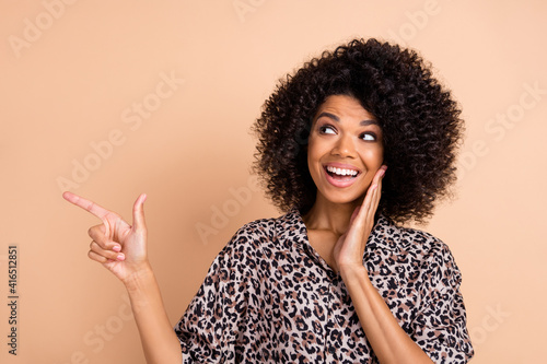 Photo of young afro woman happy smile look point finger empty space ad promo advise choose isolated over beige color background photo