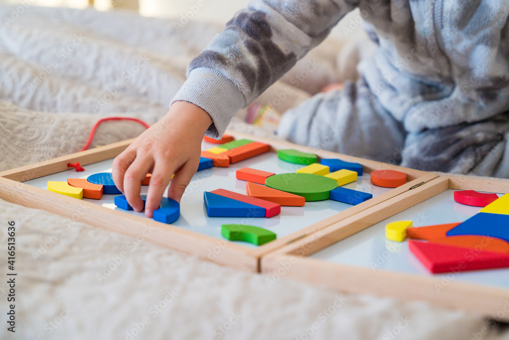 Little toddler plays on the bed in a wooden magnetic constructor, preschool child learning at home to make mosaic. Early development. Playing with chikldren during coronavirus outbreak. Little toddler plays on the bed in a wooden magnetic constructor, preschool child learning at home to make mosaic. Early development. Playing with chikldren during coronavirus outbreak.