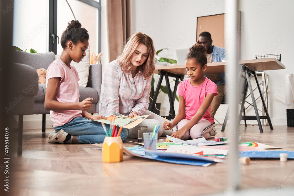 Caucasian woman watching how her multiracial daughters creating pictures Caucasian woman watching how her multiracial daughters creating pictures