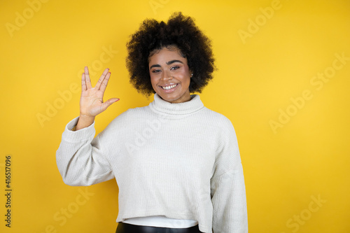 African american woman wearing casual sweater over yellow background doing star trek freak symbol