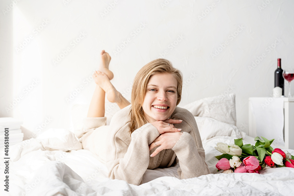 Happy woman lying on the bed wearing pajamas holding tulip flowers bouquet Happy woman lying on the bed wearing pajamas holding tulip flowers bouquet