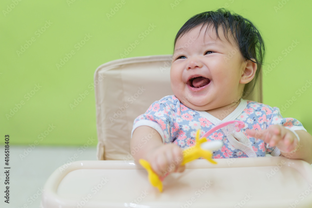 Asian happy baby eating banana on a table in the kitchen. Cute newborn baby practice to try eating food by herself on a table. Asian happy baby eating banana on a table in the kitchen. Cute newborn baby practice to try eating food by herself on a table.