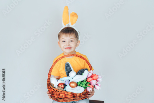 A boy in a bunny costume holding a large basket with Easter eggs and tulips. Preparation for the holiday
